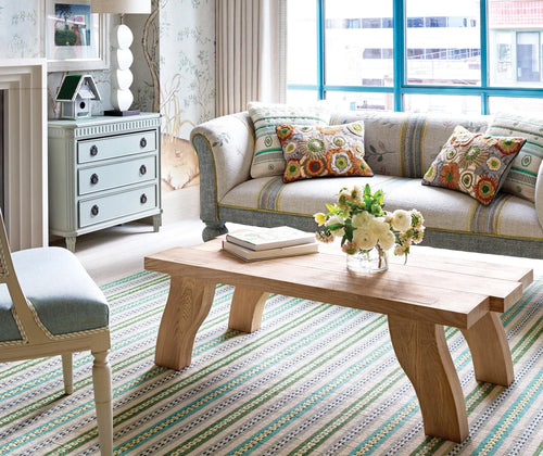 Kit Kemp's Spring Bush Cushion, in green is shown dressed on a sofa, with bramble in natural