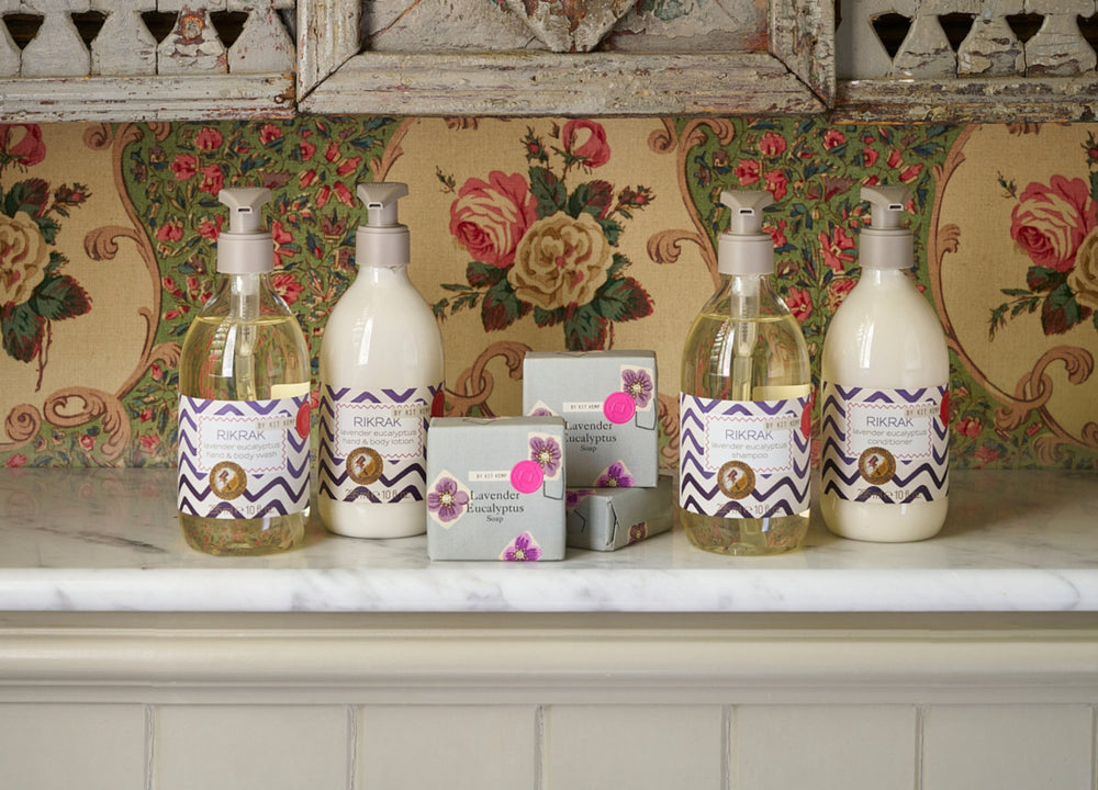 Lifestyle image of lavender body wash and lotion, shampoo and conditioner presented on a white marble shelf, in front of a sage green decorated shell box.