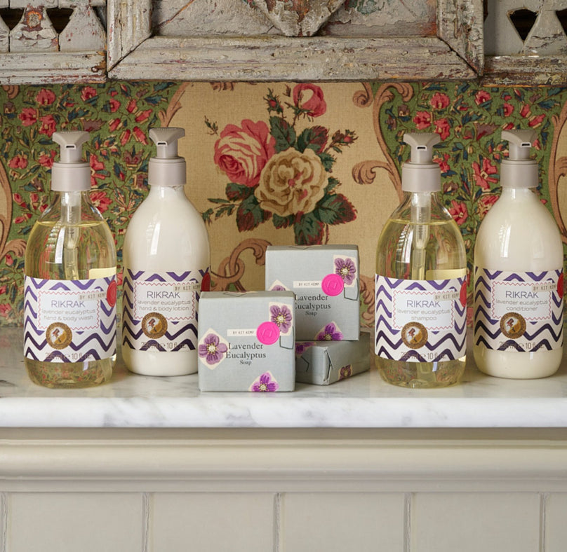 Lifestyle image of lavender body wash and lotion, shampoo and conditioner presented on a white marble shelf, in front of a sage green decorated shell box.