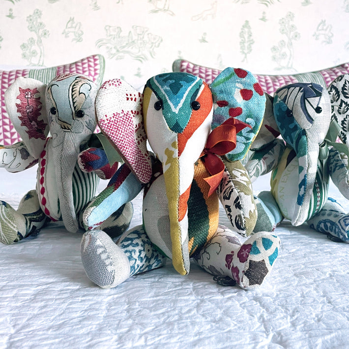 Jambo the elephant patchwork toy, is pictured in a combination of printed and embroidered fabrics all on a natural base, with highlights of pink, blues and duck egg greens, to make a truly unique cuddly toy.