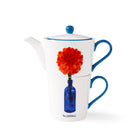 The Doodles tea for one , features a stackable white t pot illustrated with a blue bottle, and large red chrysanthemum bloom, and the Tag-line Blooming , which sits above the base mug, in navy and white.