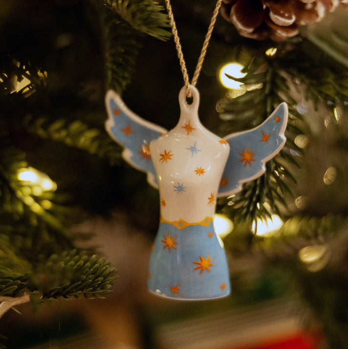 The elegant Angel Mannequin fine china Ornament from the exclusive Kit Kemp for Spode collection. This unique ornament features a white bodice and blue skirt pattern adorned with vibrant orange and gold stars. Its sophisticated design and connection to Kit Kemp's aesthetic make it the perfect collectible gift for fans of Firmdale Hotels, adding a touch of designer whimsy to any Christmas tree.