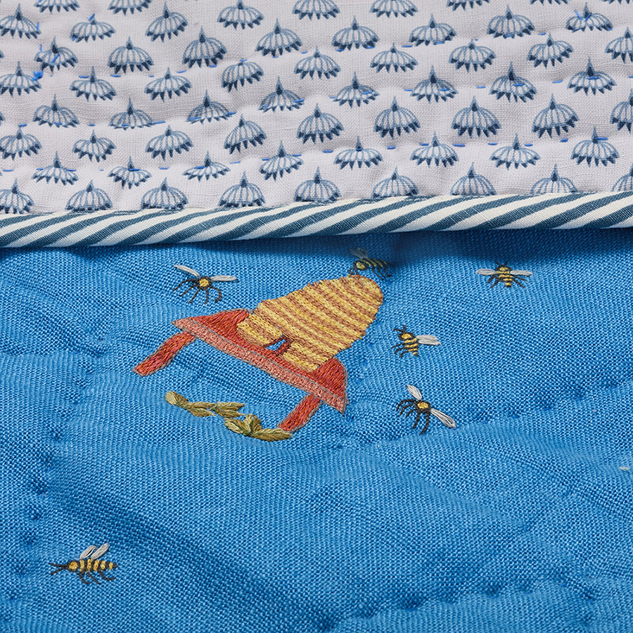 Close-up of the Buzz Off Quilted Bedspread in Blue, showcasing intricate embroidered bee and floral motifs on quilted linen with exceptional craftsmanship by Kit Kemp for Chelsea Textiles.