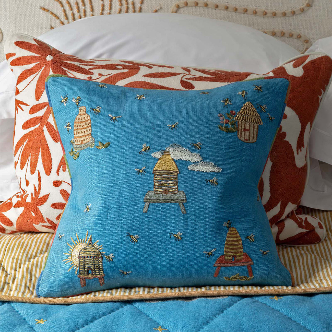 Layered Buzz Off cushion on bed with terracotta floral pattern on white, inspired by nature and weekends in gardens and countryside.