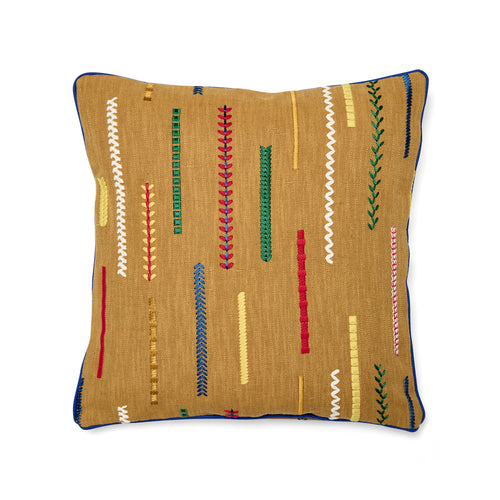 45cm x 45cm (18in x 18in) Kit Kemp Design Studio cushion in mustard yellow. The design features "Cayeres" fabric by Élitis, showcasing broken, multicoloured embroidered lines in shades of red, blue, and green on a rustic canvas. The cushion is finished with a sharp, contrasting cobalt blue piped edge.
