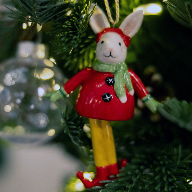 Playful Christmas Bell Bunny fine china Ornament wearing an adorable elf outfit. The bunny features a bright red jacket, a green scarf, and dangling yellow and red legs that bring a touch of whimsy and fun to your holiday decor. A charming, quality gift for collectors and rabbit lovers.