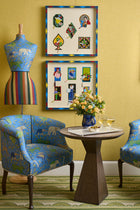 A table of drinks on a geometric carpet with 2 tub chairs either side and a fabric mannequin the in background. 