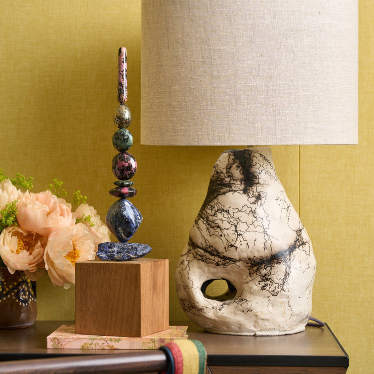 A Totem sculpture made from crystal gemstone with table lamp and handle chair against a yellow wall 