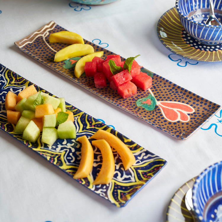 ceramic tray with bananas, watermelon, and melon on a decorative plate with a bowl of oranges in the background.