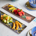 ceramic tray with bananas, watermelon, and melon on a decorative plate with a bowl of oranges in the background.