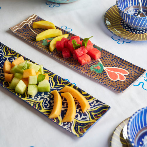 ceramic tray with bananas, watermelon, and melon on a decorative plate with a bowl of oranges in the background.