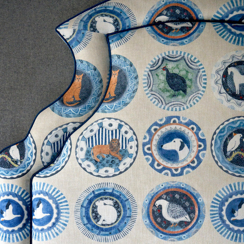 Close up detail on Ellie headboard edge with blue piping and Robina's Dinner Party fabric, featuring playful animal characters, including dog, cat, lion, guinea fowl, horse, rabbit and birds. 