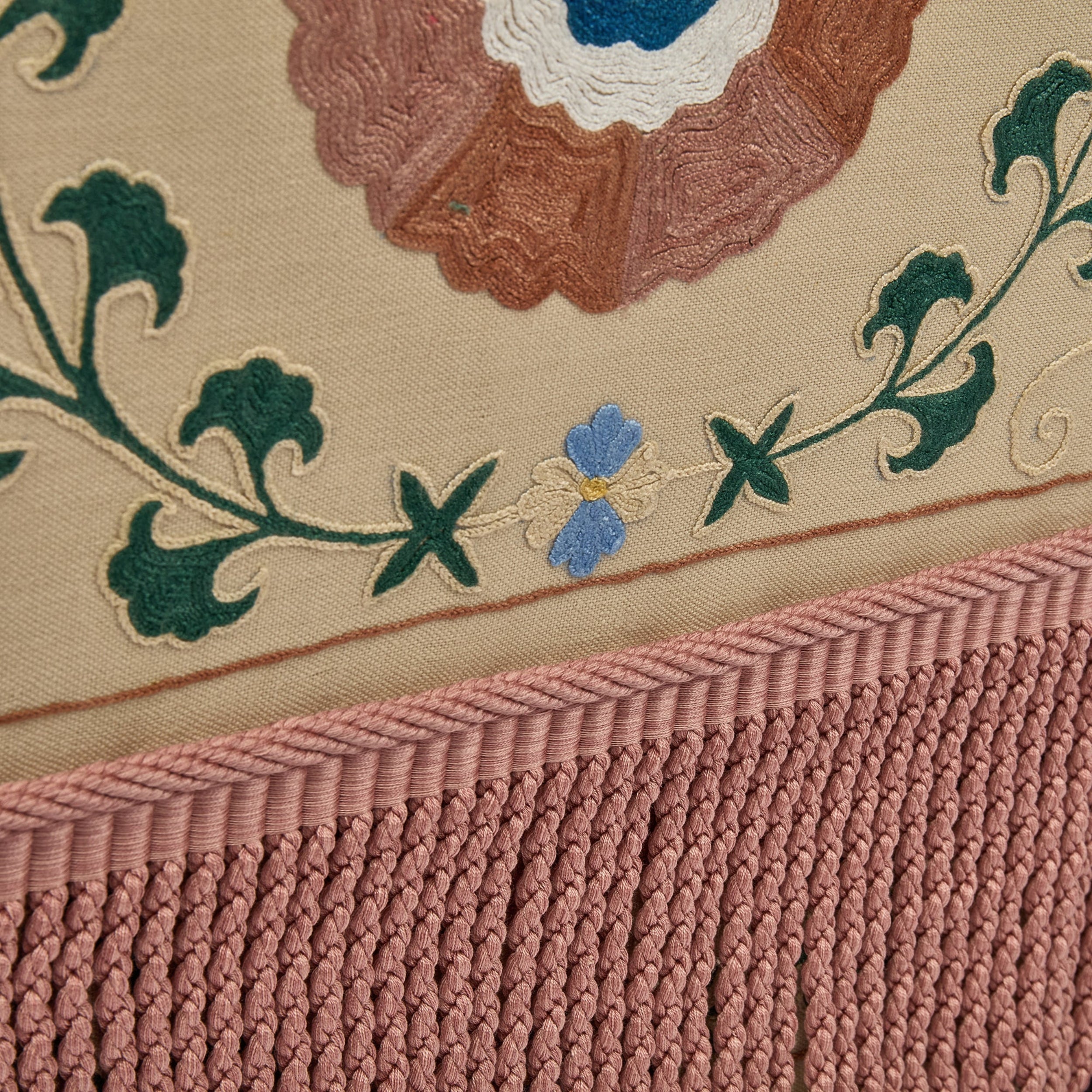 Close-up of embroidered fabric with floral design and fringed edge.