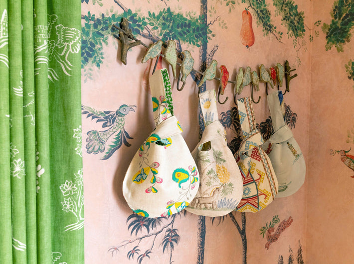 A series of patterned fabric bags are hung on a decorative coat rack against a patterned wallpaper featuring trees and birds