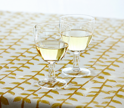 Two clear stemmed glasses filled with white wine on a patterned tablecloth.
