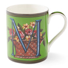 The blue M on this emerald green mug sits among a basket overflowing with yellow and red flowers.