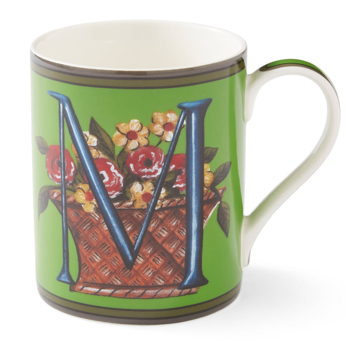 The blue M on this emerald green mug sits among a basket overflowing with yellow and red flowers.