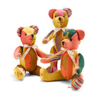 A luxury patchwork teddy bears featuring a sophisticated mix of woven textiles. Details include multi-coloured striped knit paws, a delicate cream satin ribbon tied at the neck, and an authentic numbered stamp on the foot, highlighting its limited-edition, collectible quality.