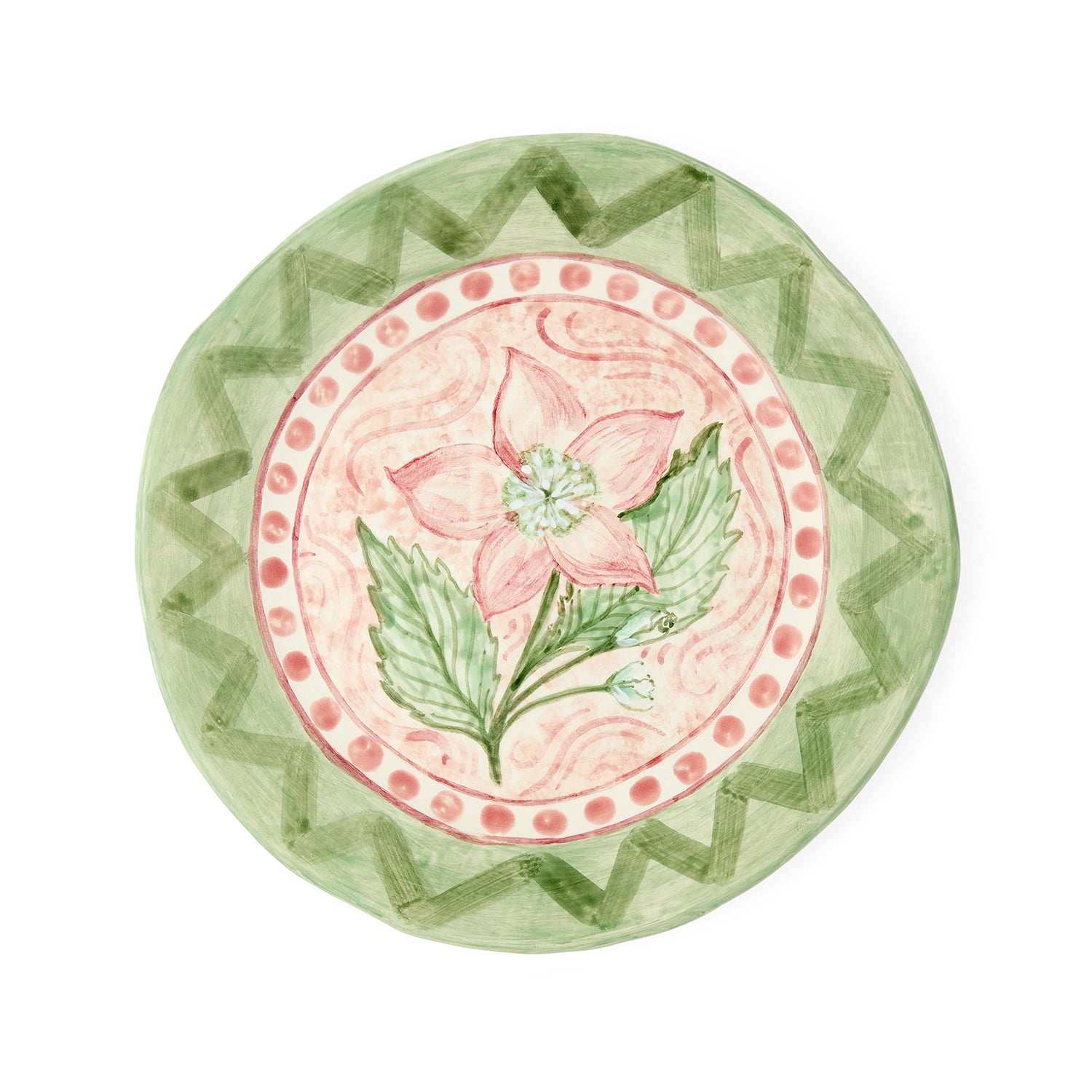 Hand-painted "Pink Hellebores in the Garden" ceramic plate by Sasha Compton for Shop Kit Kemp, featuring a central pink floral motif encircled by a dusty rose dotted rim and a wide green geometric zigzag pattern. 