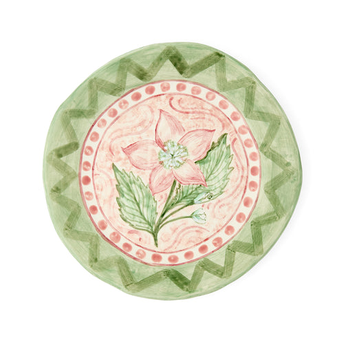 Hand-painted "Pink Hellebores in the Garden" ceramic plate by Sasha Compton for Shop Kit Kemp, featuring a central pink floral motif encircled by a dusty rose dotted rim and a wide green geometric zigzag pattern. 