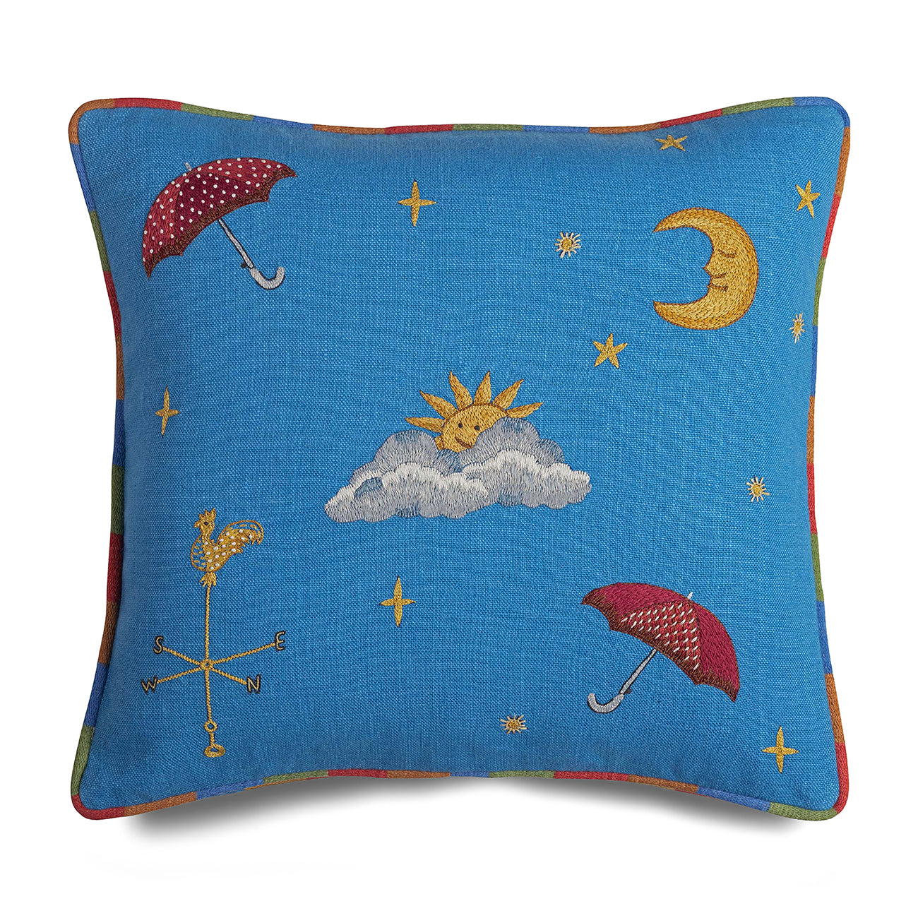 Edged in rainbow piping, the Rain Or Shine cushion with embroidered sun, moon, clouds, and umbrellas, on blue linen background. 
