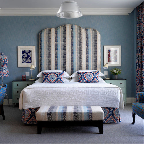 Kit Kemp's 'Ruby' headboard is a bold structural shape with its shallow triple curved top, upholstered with a Kit Kemp's signature fabric designs 'Bookend' for Christopher Farr Cloth.