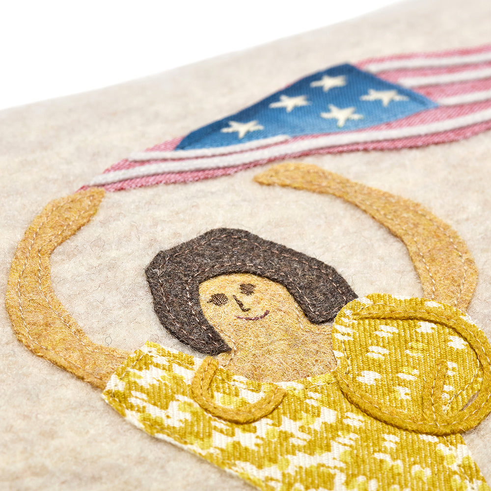 Close-up of the artisan-made appliqué, showing the lady in a yellow dress waving a flag, hand-stitched on soft 100% Chamonix wool.