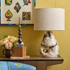An organic-shaped, hand-sculpted ceramic table lamp base by artist Daniel Clarke for Shop Kit Kemp. The lamp features a raku-fired finish, and it is paired with a neutral drum linen lampshade and styled on a Kit Kemp desk.