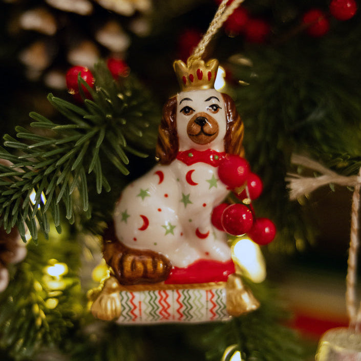 Festive fine china Christmas tree decoration in the shape of a sitting Staffordshire Dog. Inspired by Kit's patchwork animals, this stylish ornament features bright patterns (red crescent moons, green stars) and gold accents, making it a unique and delightful addition to any Christmas tree or a perfect gift for a dog lover.