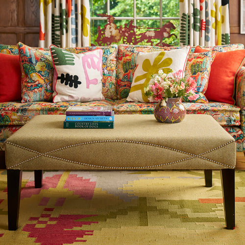 Colorful sofa with patterned cushions and a matching ottoman in a room with floral curtains.