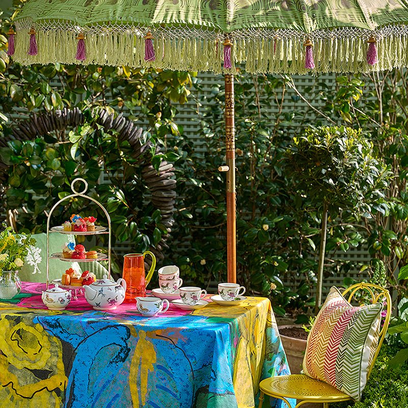 Kit Kemp Mythical Creatures fine china and bright napkins styled on the Sunshine tablecloth, showcasing how the specialist cotton treatment protects against spills.