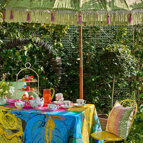 Kit Kemp Mythical Creatures fine china and bright napkins styled on the Sunshine tablecloth, showcasing how the specialist cotton treatment protects against spills.
