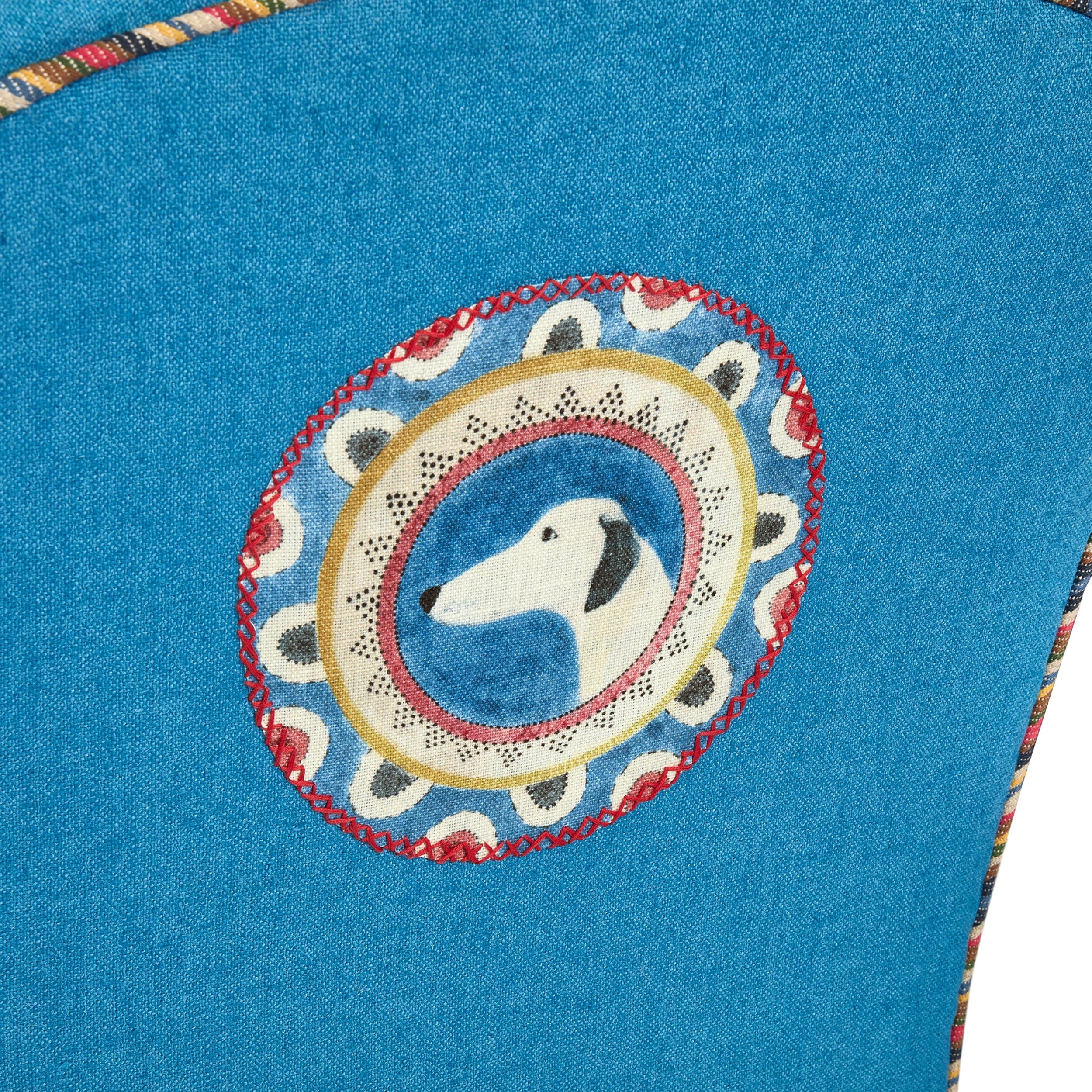 Embroidered design of a dog's face on blue fabric with decorative border