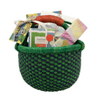 A woven African basket with a leather handle, containing Kit Kemp notebook, A5 notecards, Firmdale pencils box, and a RikRak wheatgrass candle. A perfect present for a writing enthusiast and a self-care gift.