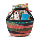 A colourful Shop Kit Kemp woven basket with a leather handle, containing a Mythical Hallway  jigsaw puzzle, a Mind Over Matter mug, and a Mythical Creatures tea caddy tin, presented as a gift set.