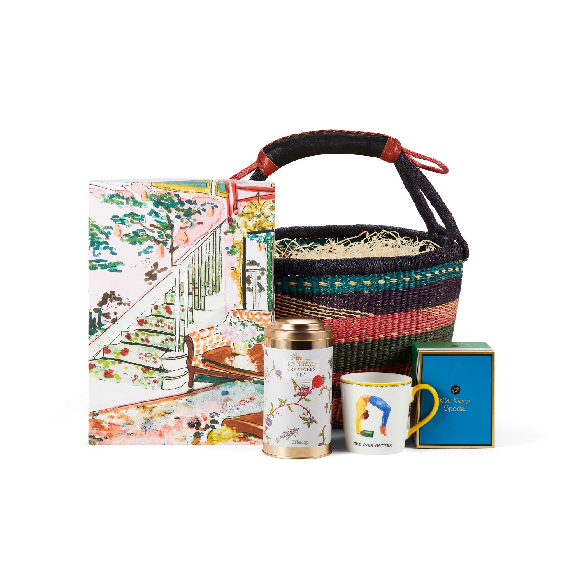 A colourful Shop Kit Kemp woven basket with a leather handle, containing a Mythical Hallway jigsaw puzzle, a Mind Over Matter mug, and a Mythical Creatures tea caddy tin containing 20 tea bags, a perfect gift for winter and cosy days.