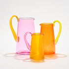 Three hand-blown glass jugs in vibrant shades of pink, orange, and yellow with contrasting colour handles, perfect for adding Kit Kemp joyful design to any table-setting.