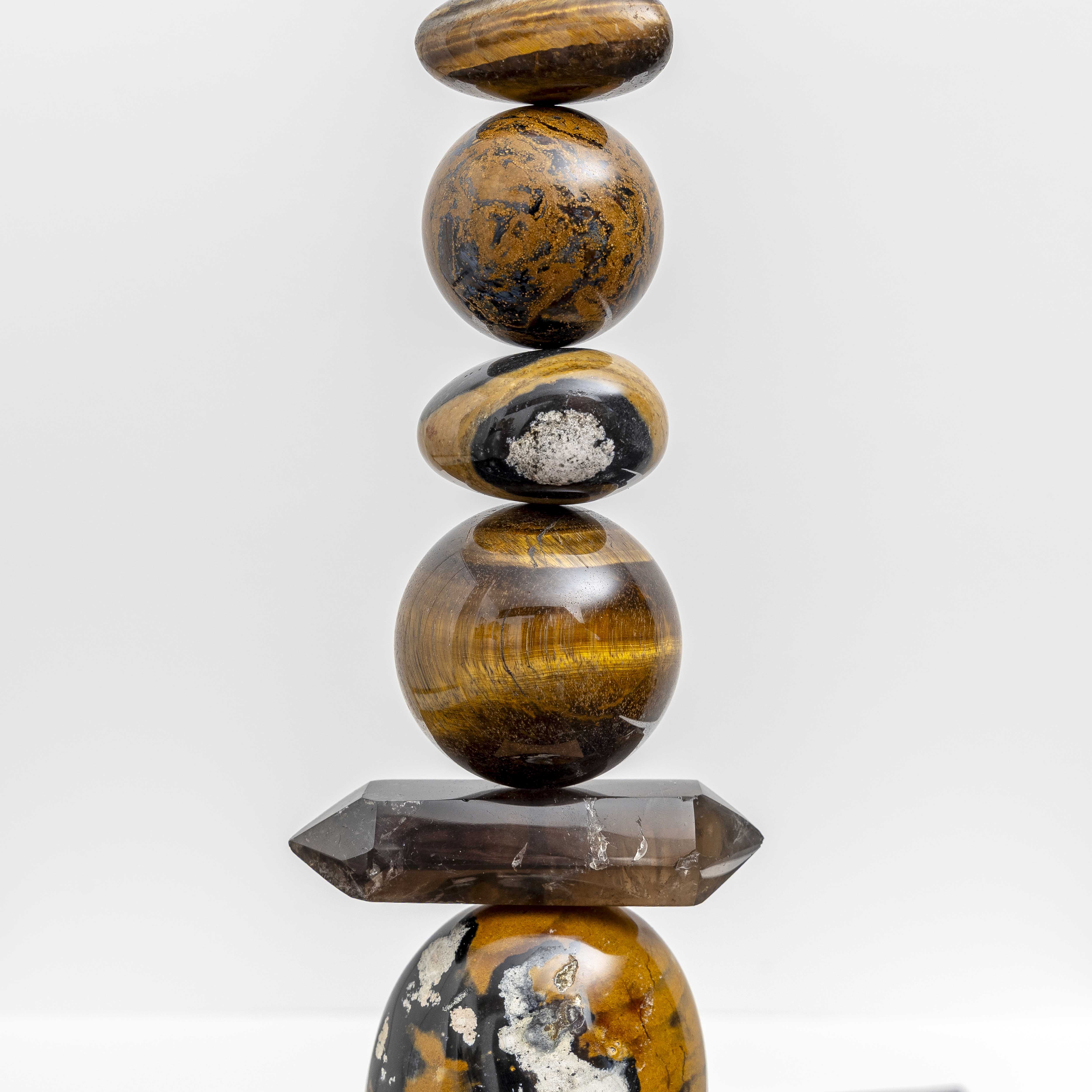 Ancient Sands II is entirely unique and made from the following precious crystal stones: From the top – 2 pieces of Yellow Jasper, Tigers Eye, Pietersite sphere, Yellow Jasper, Tigers Eye sphere, Smokey Quartz rod and a large form of Yellow Jasper.  All sitting on an Iroko wood plinth. Size H43cm W11.5cm D11.5cm includes base.
