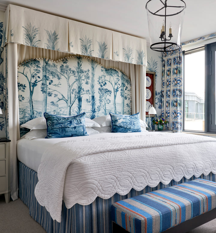 Firmdale bedroom featuring the Tall Trees blue headboard, and wallpaper, end of bed stool and valance in tones of blue and grey