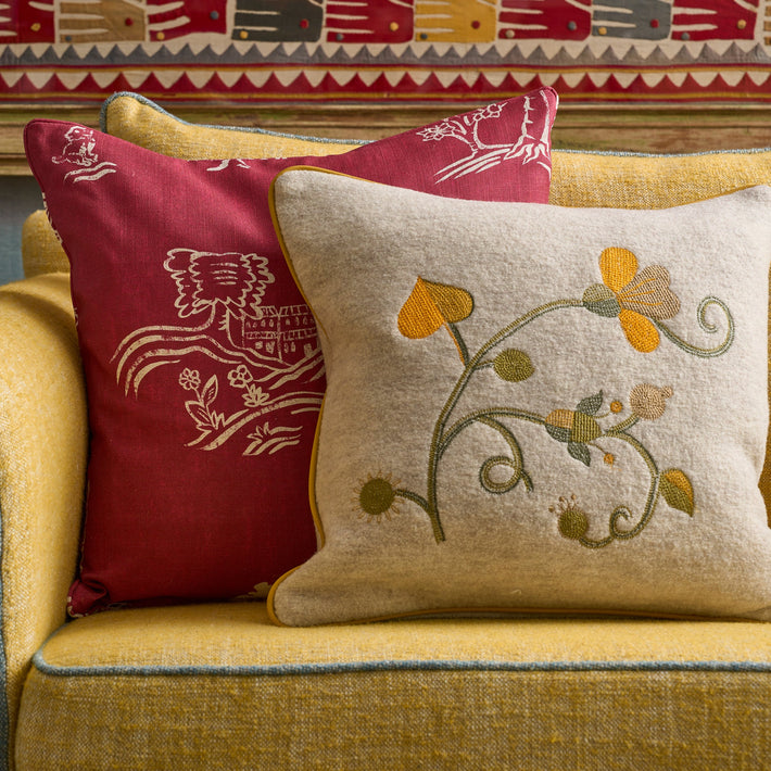 The Araminta cushion is shown lifestyle on a yellow and pale blue Willow sofa, with a Friendly Folks cushion in red 