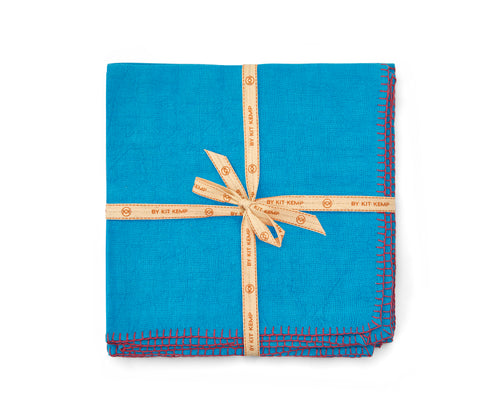 A stack of beautifully soft Italian linen 50x50 napkins, in bright turquoise linen hand-stitched in pink blanket-stitching around the edges, sold in packs of 6, shown stacked and tied with a natural calico ribbon.