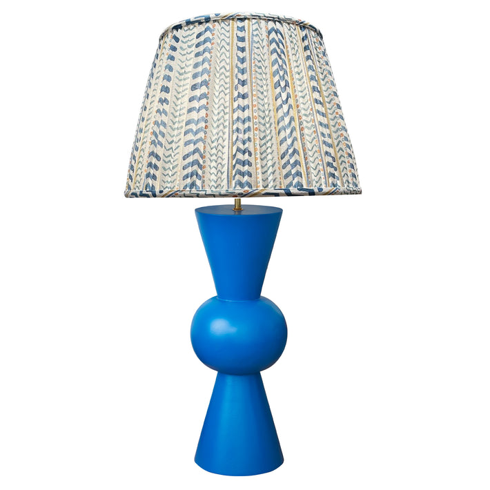 Kit Kemp's Blue Bow Lamp, makes for a striking lamp with its large sphere centre and conical upright tapered ends in a deep royal blue, this lamp base is bold in both form and colour. Topped with the gathered shade in Kit's new fabric Wriggle Room, with its white ground and zig zag stripes, in shades of blue and yellow.