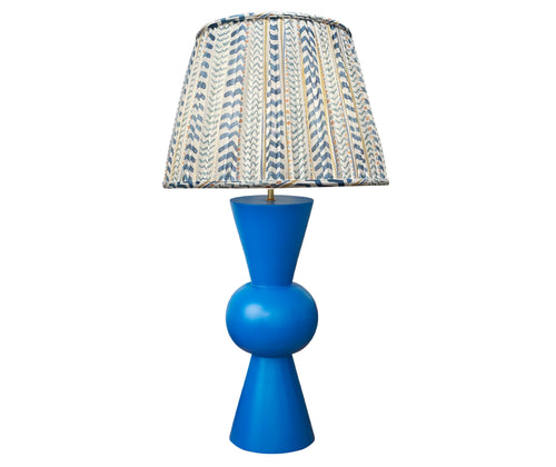 Kit Kemp's Blue Bow Lamp, makes for a striking lamp with its large sphere centre and conical upright tapered ends in a deep royal blue, this lamp base is bold in both form and colour. Topped with the gathered shade in Kit's new fabric Wriggle Room, with its white ground and zig zag stripes, in shades of blue and yellow.