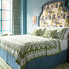 Button in olive is shown dressing a bed , which is also covered with the Knightwood bedspread, and pillow cases, in a blue room.