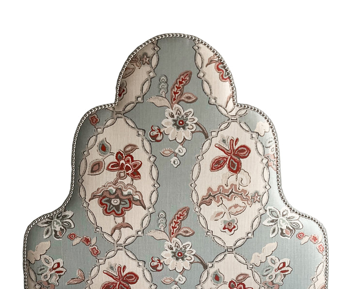 The Flora head board, is a tall upholstered headboard with 3 prominent arches, reminiscent of a Victorian Jelly Mould, pictured here upholstered in Kit Kemps Blue Chain Stitch material, with its abstract red, beige and pink abstract floral design, surrounded in ornate oval-like framework outlines.