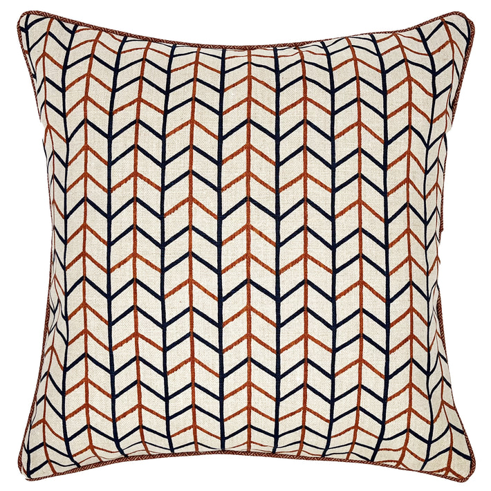 This image shows a decorative square cushion with a geometric pattern. The design features a series of interlocking lines in blue and terracotta orange, The background of the pillow appears to be off-white. The edges of the pillow are neatly finished with a piping of a red parquet fabric