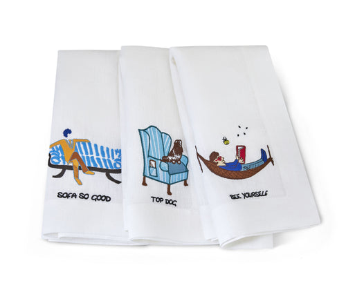 The doodles white linen embroidered napkins, shown laid out to display the 3, individual embroidery designs including with the top dog, blue and white kit chair, with a brown and white spaniel, a reclining man on a large blue and white stripped sofa, , and our man in a brown hammock, illustrating the Bee Yourself, tag line.