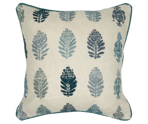 The image displays a cushion with a botanical design. The pattern features stylized stitched representations of fern-like plants in two colors, dark blue and a lighter blue grey, set against a neutral beige fabric background. 