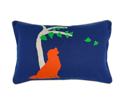 The image displays the front of the Labrador cushion, a decorative cushion with a vibrant design. The cushion's background is a bright blue, and it features a white stylized tree with green leaves. Next to the tree, there is a prominent silhouette of a Labrador dog in orange colour. The pillow's rectangular shape and colorful artwork give it a playful and modern aesthetic, intended to serve as a decorative element in a home