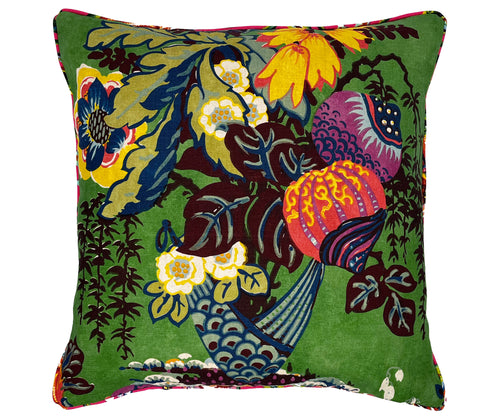 This image shows the front of the Fairbanks cushion in green with an intricate and colorful floral design on a green background. The design features a variety of stylized flowers and leaves in vivid colors such as yellow, blue, and orange. The edges of the pillow are trimmed with a pink piping, adding a subtle contrast to the bright and busy main design.